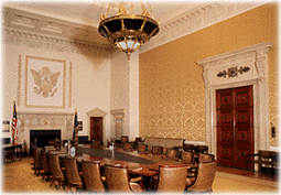 Photograph of the unoccupied Board Room showing long table with 20 high-backed chairs around it, chandelier overhead, and fireplace at one end